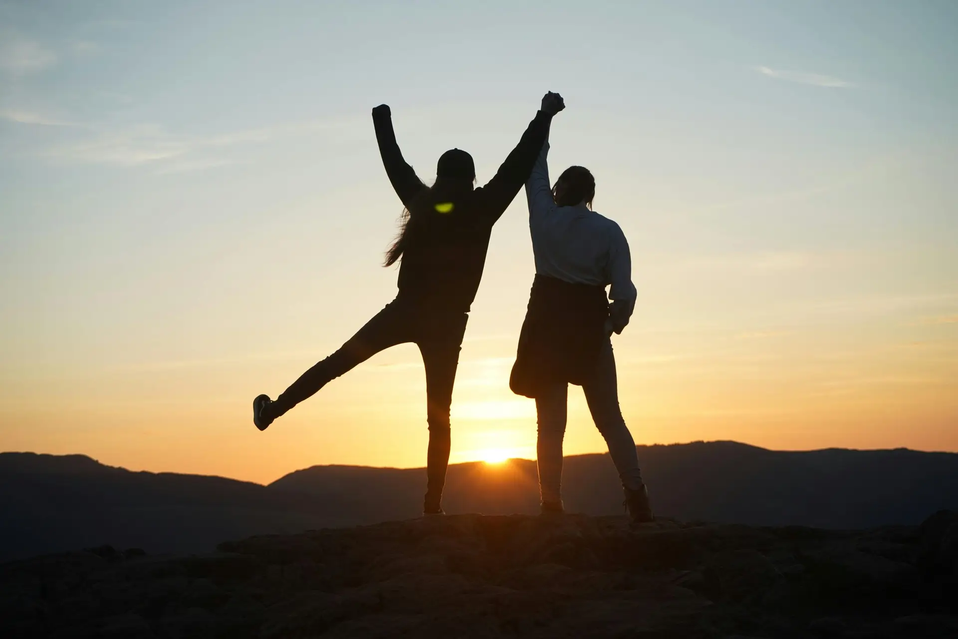 A couple celebrates together on a mountain hike with a stunning sunset backdrop in England.